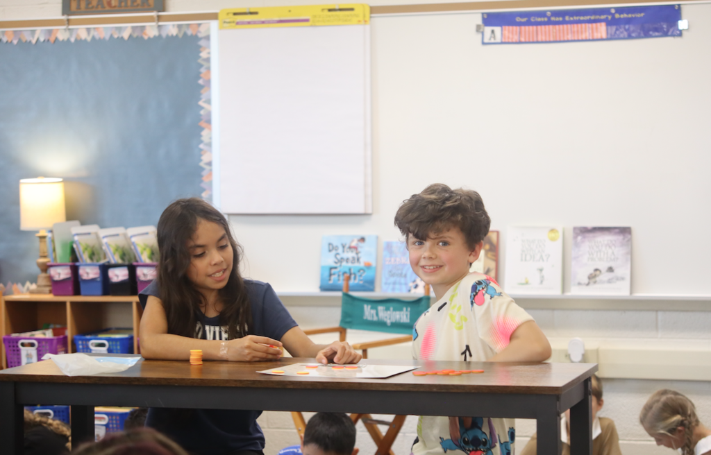 little boy and girl sitting at a table doing math, boy smiling at camera