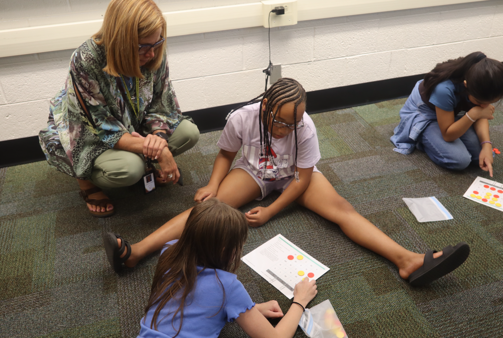 teacher helping two girls with math card 