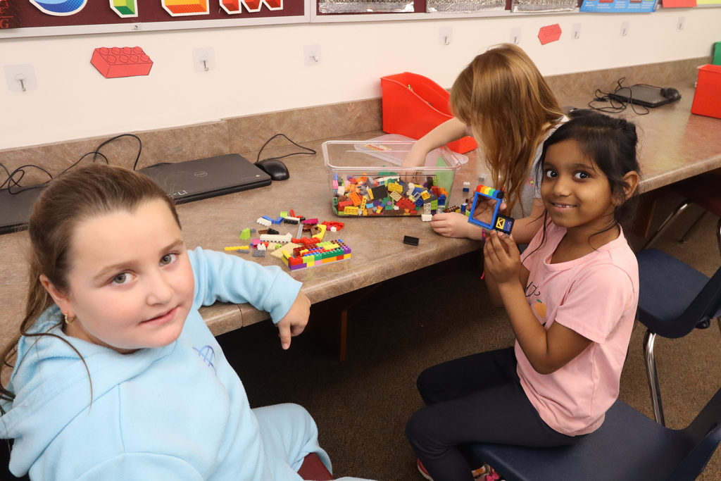 two girls looking at the camera with their legos, one looking in the box