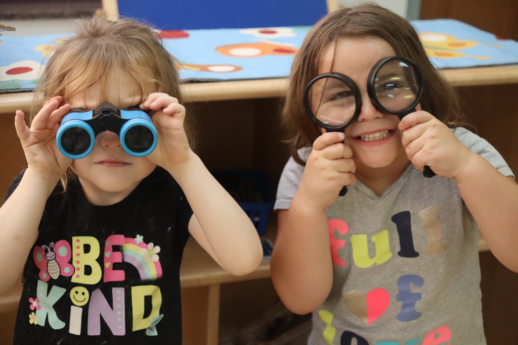 two little girls, one looking into binoculars, one looking into magnifying glasses
