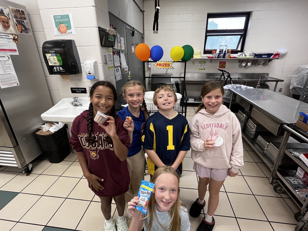 give kids standing in front of balloons in cafeteria holding treats
