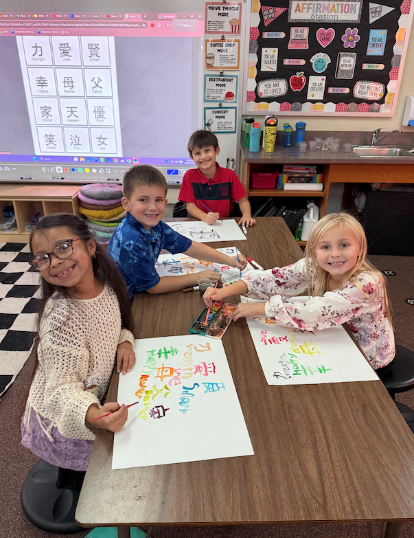 4 kids sitting at desk working on chinese characters