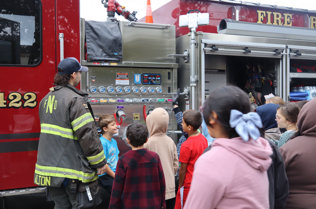 group of students looking at fire truck with firefighter