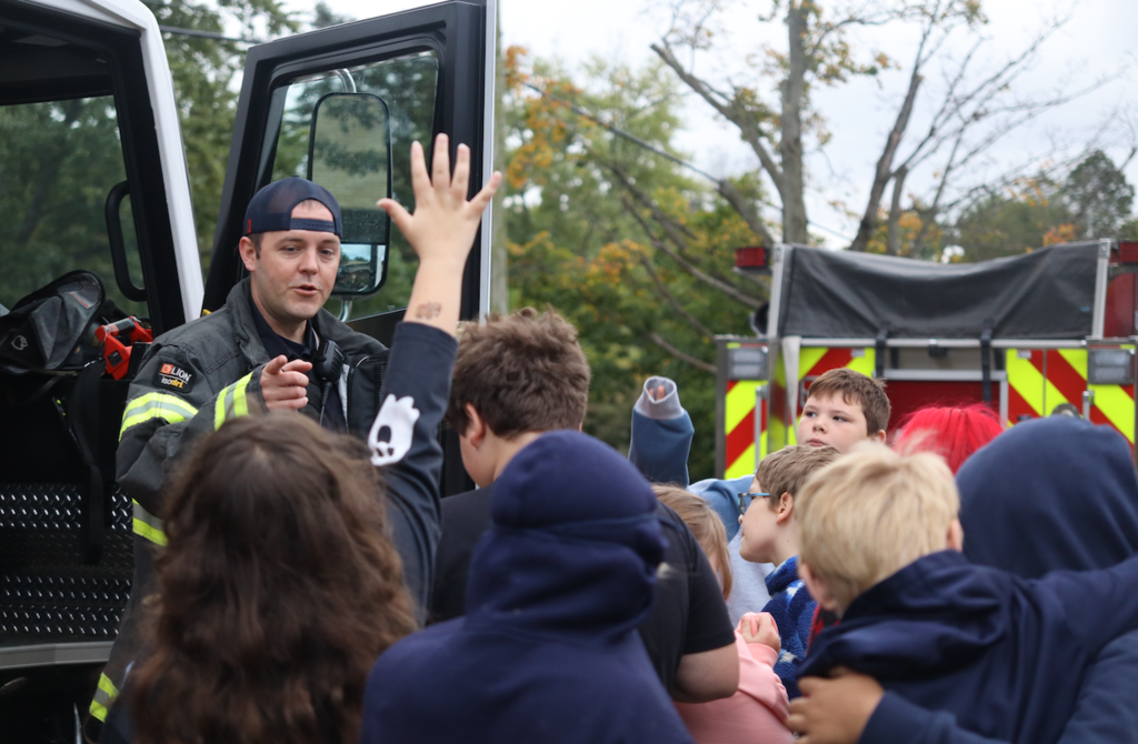 group of students looking at fire truck with firefighter