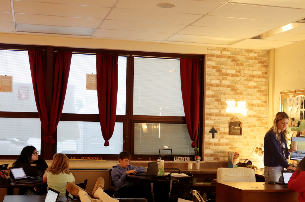kids sitting at a desk in classrooms, teacher standing at desk