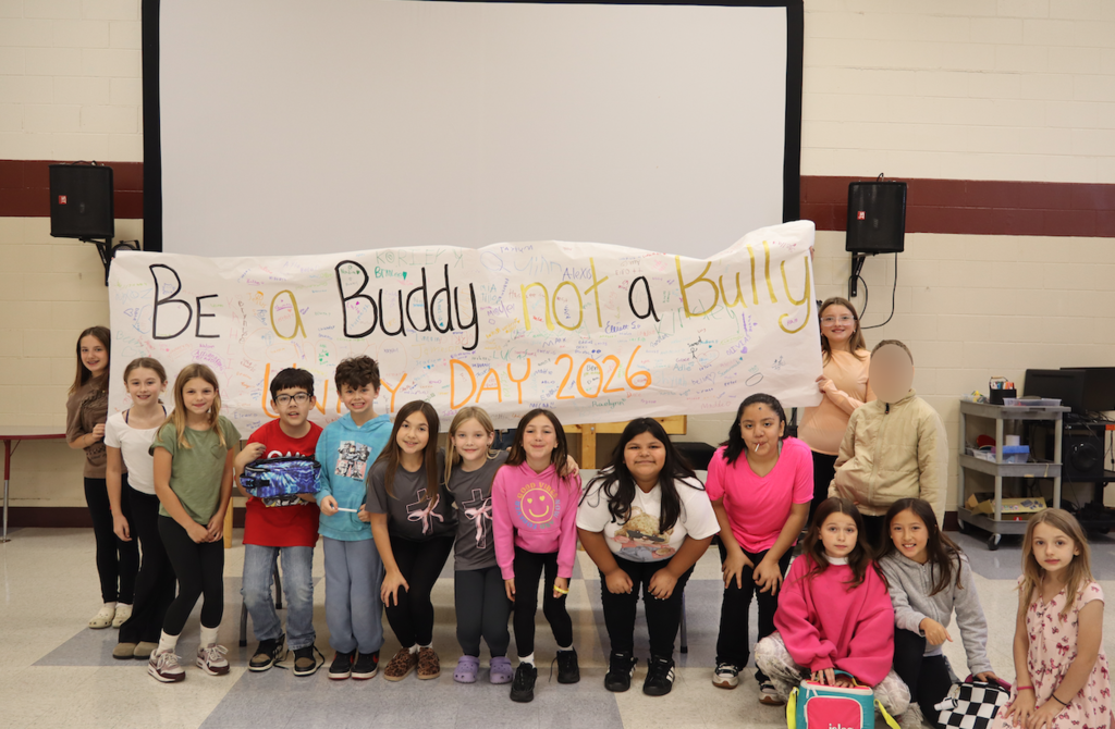 kids standing in front of a banner that says "be a buddy not a bully"