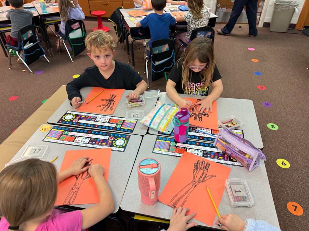 group of kids sitting at desk with hand drawings