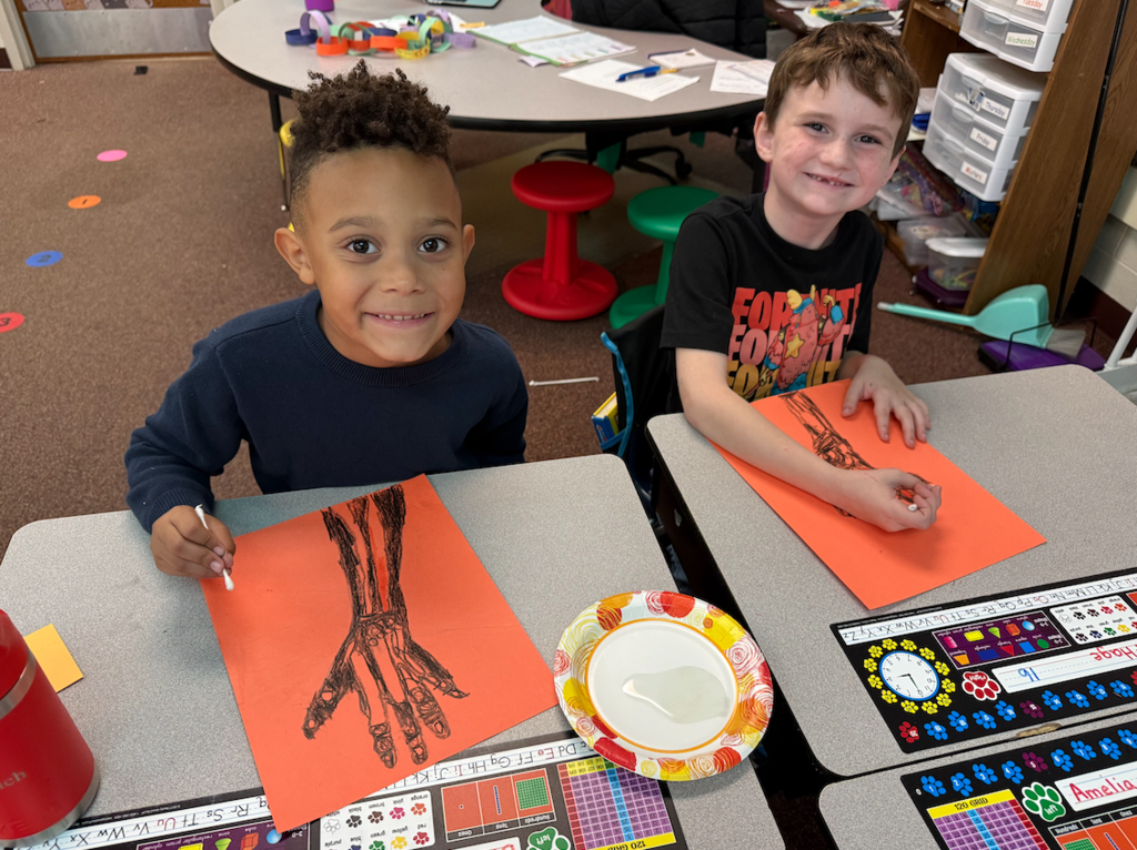 two little boys sitting at desks with hand drawings