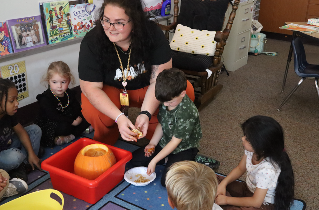 kids and teacher on the floor removing seeds from pumpkin