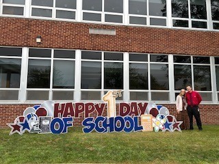 two people stand next to first day of school sign