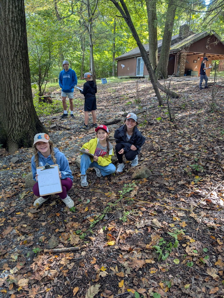 students smiling showing off clipboard of activity in the woods at camp