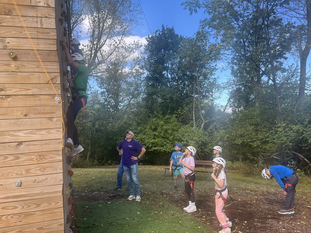 students cheer on another student working on the climbing wall