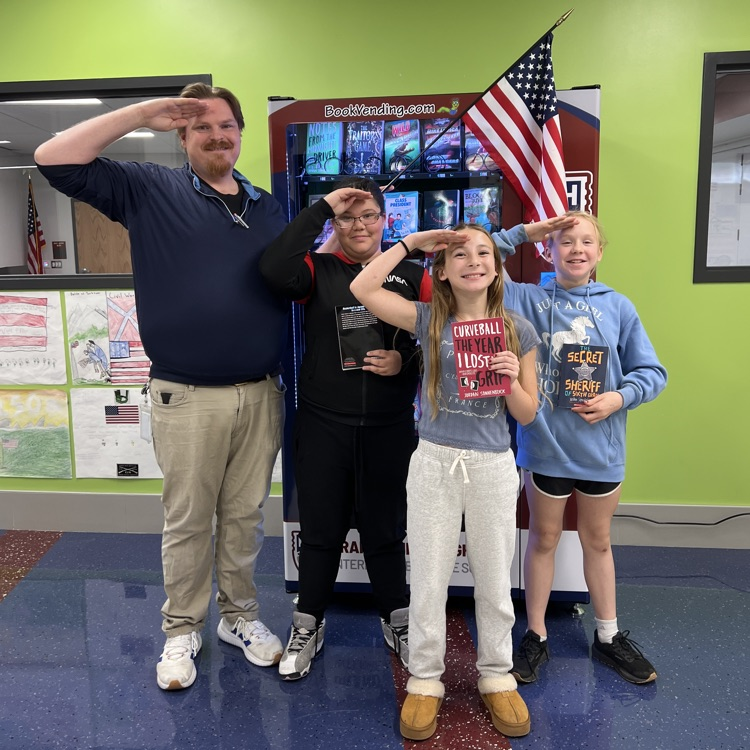 three students stand with teacher next to book vending machine