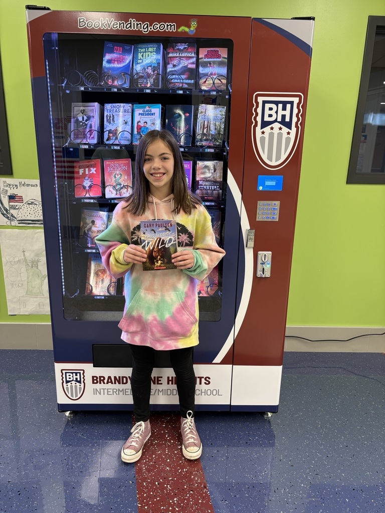 student stands with book in front of book vending machine