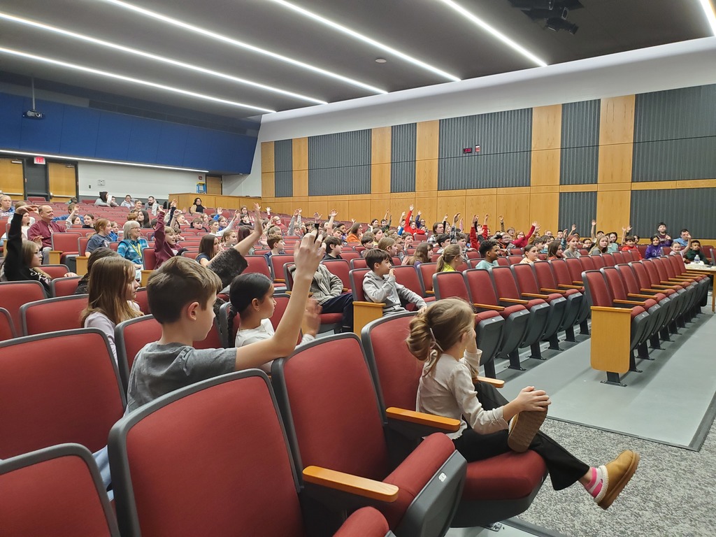 students sitting in auditorium seats, many with their hands raised