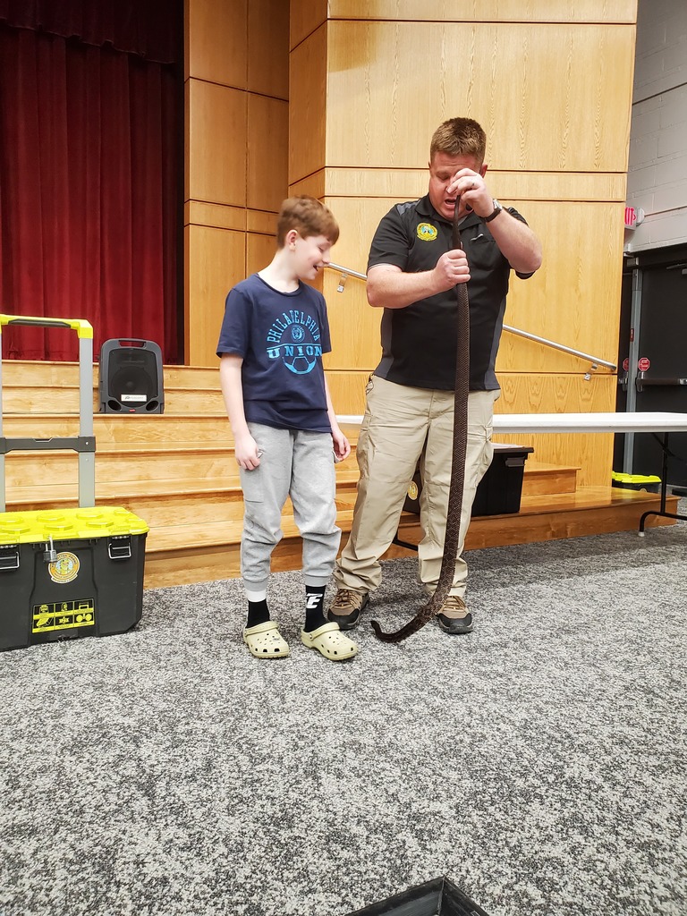 student stands next to a man holding a snake to compare height