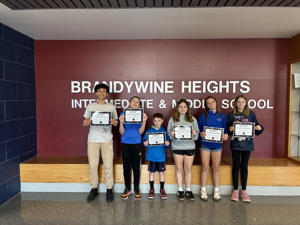 six students stand smiling holding certificates in front of a maroon wall