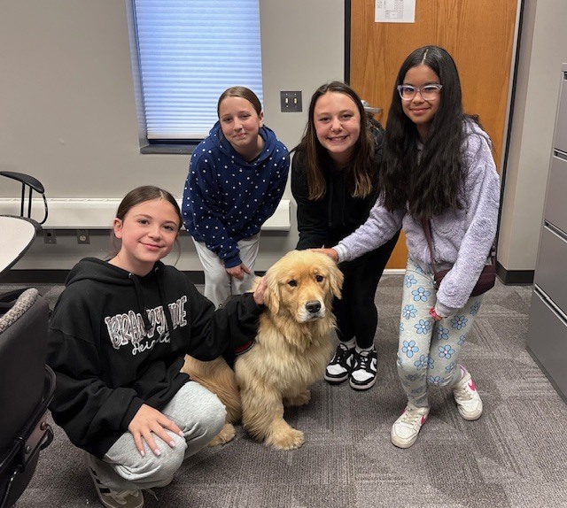 4 students pose smiling with golden retriever