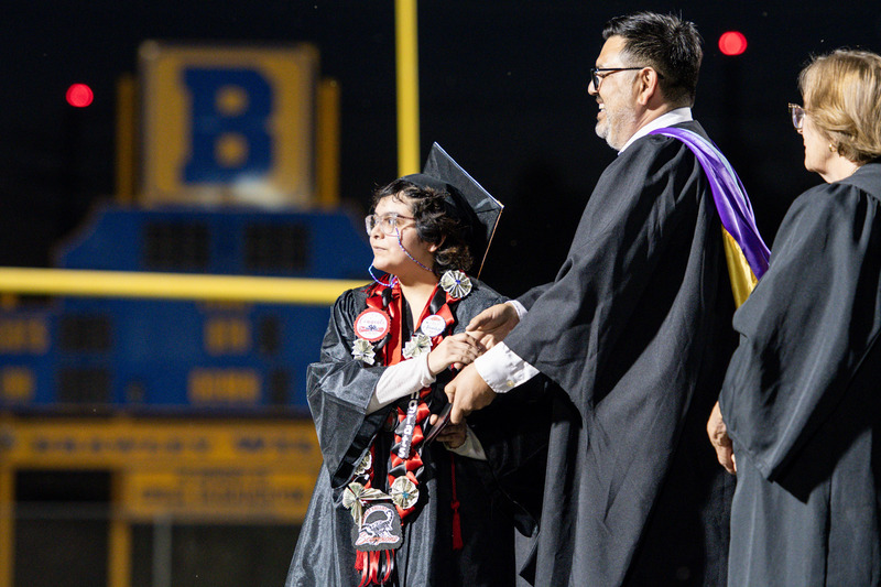 Graduates walk across graduation stage.