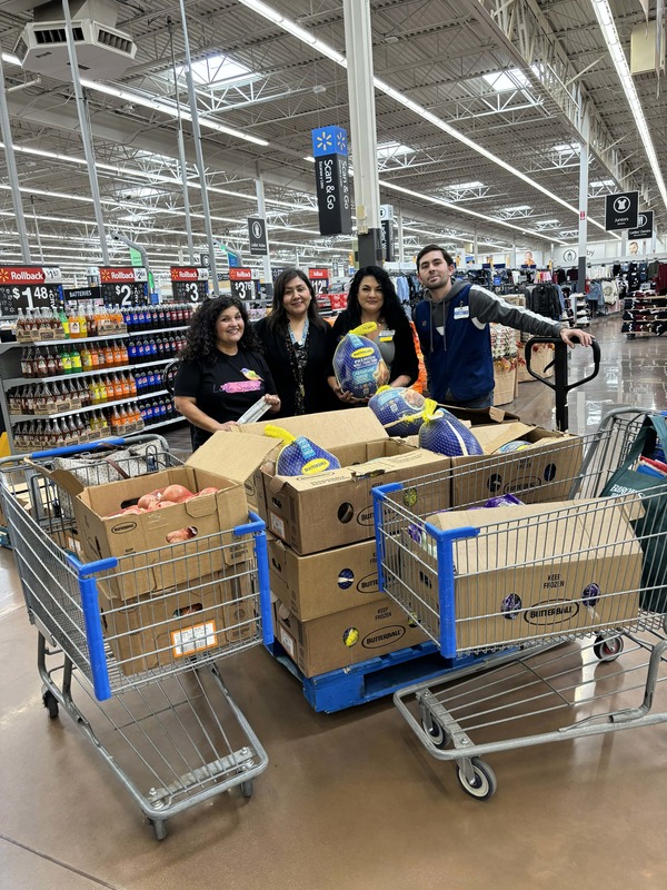 Community school coordinator poses next to walmart staff with cart of donated items.