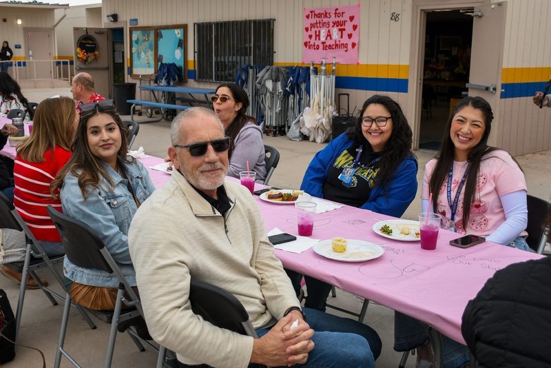 Group of four school staff smile for photo while enjoying breakfast..