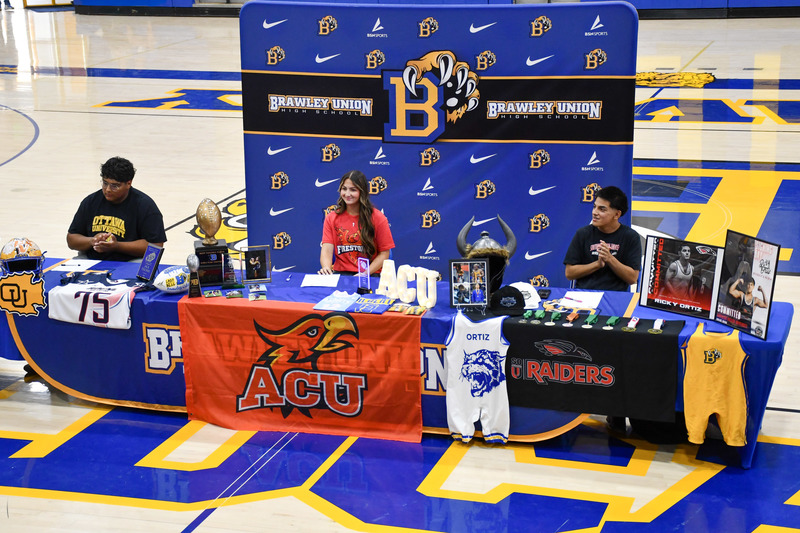 Three students sit together at the atheltic signing event