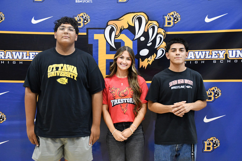 Three students sit together at the atheltic signing event