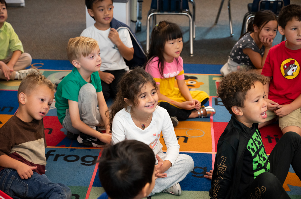 a photo of preschool age children sitting on a colorful rug