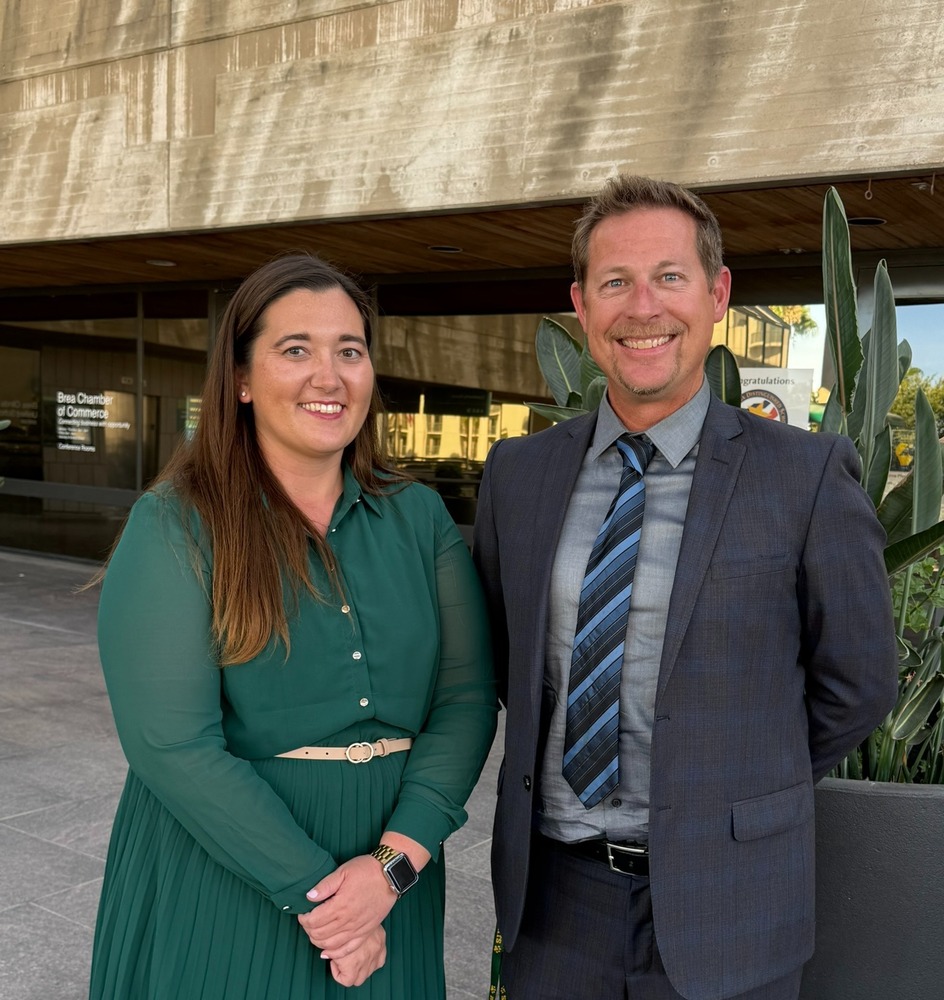 photo of nicole bear and brandon frank standing against a large planter and building behind them