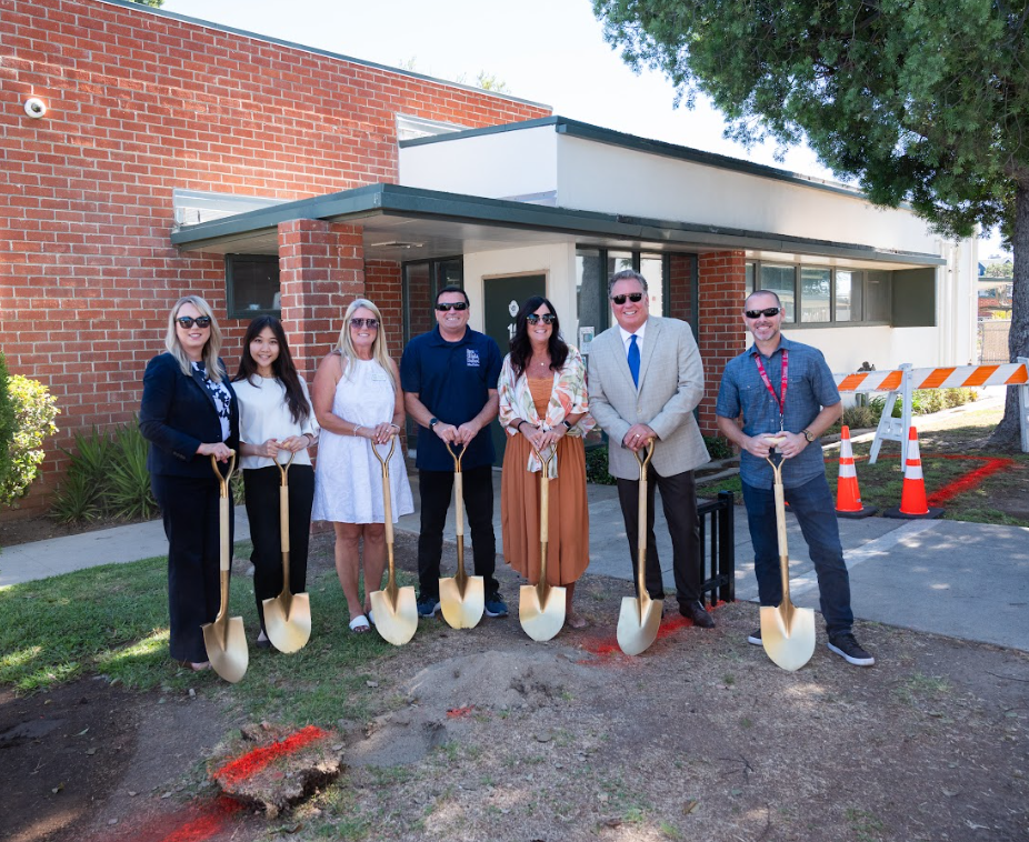 Photo of members of Cabinet and the Board of Trustees in front of brick building holding shovels
