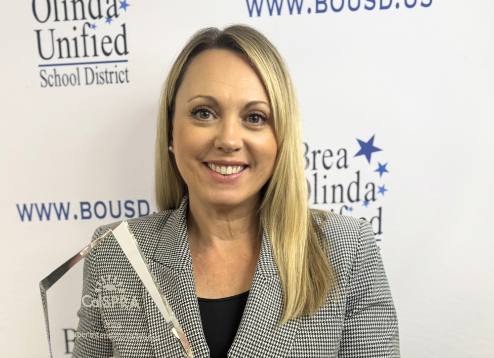 Brinda Leon holds up a glass award in front of a BOUSD backdrop