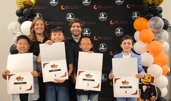 a group of student from Falcon Academy hold up certificates with balloons in the background