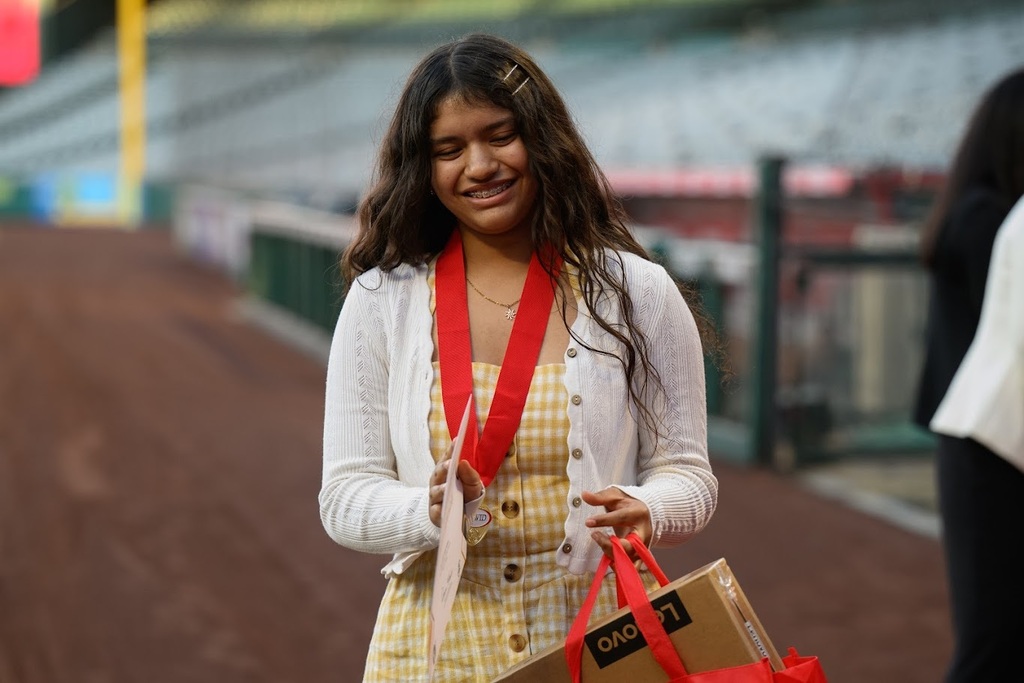 Camila looks down while holding her awards on the baseball field.