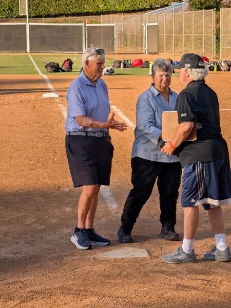 Sharen Caperton shakes hands with a gentlman dressed in black shirt and shorts on the base ball field