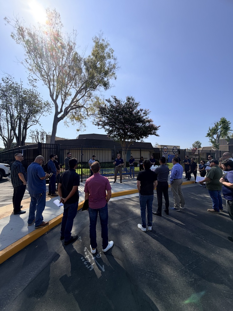 Individuals face Falcon Academy site while standing on black pavement and sidewalk