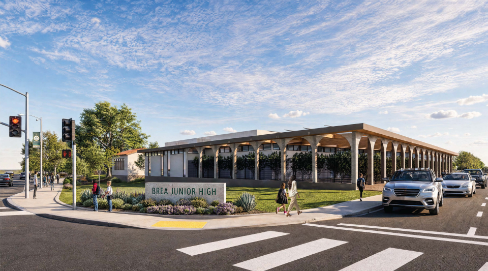 photo rendering of Brea Junior High with cars and people passing by on the road and by foot. A building with arches is visible along with a street light and sign that reads Brea Junior High