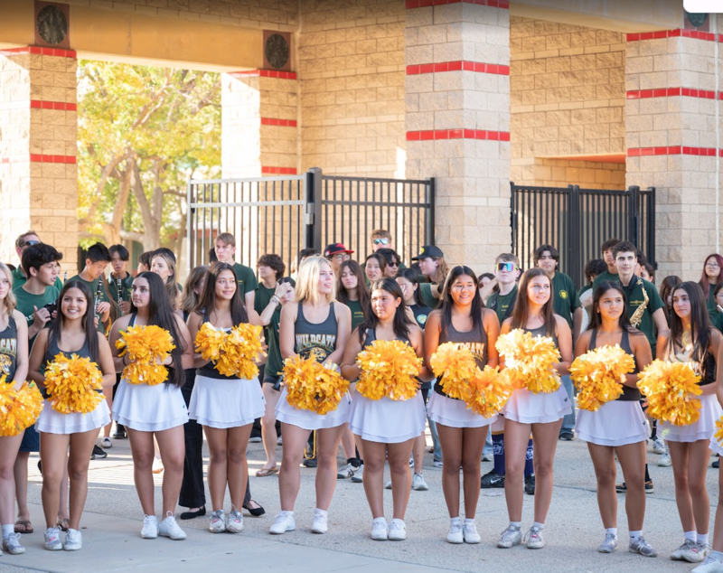 a line of cheerleaders with gold pom poms stand in front of BOHS entrance. Band members stand behind them