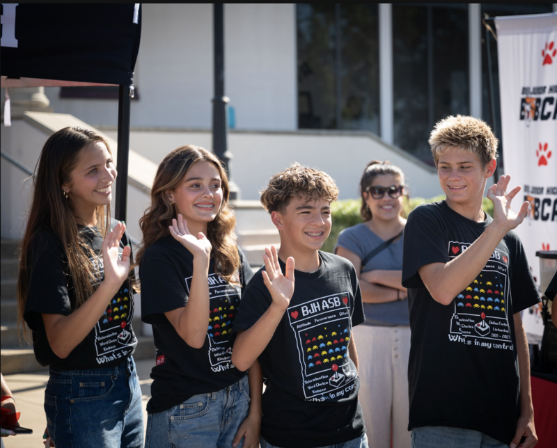 students in black t-shirts waving and smiling