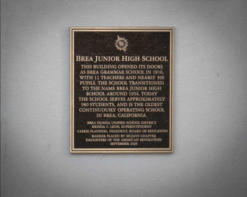 A bronze plaque with gold text against a white wall.