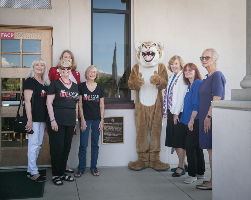 A group of older women stand near the plaque with Brea Junior High mascot