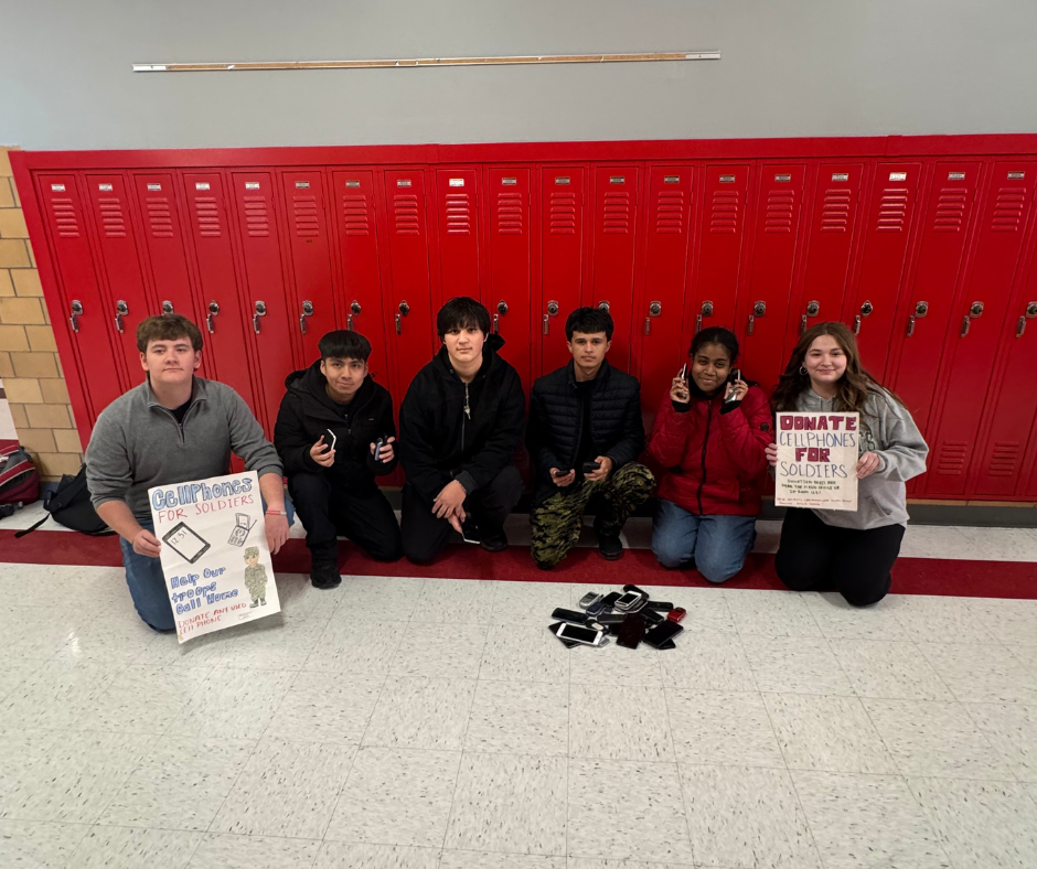 Students pose for a photo in front of red lockers at Bremen High School holding signs for Cell Phones for Soldiers.