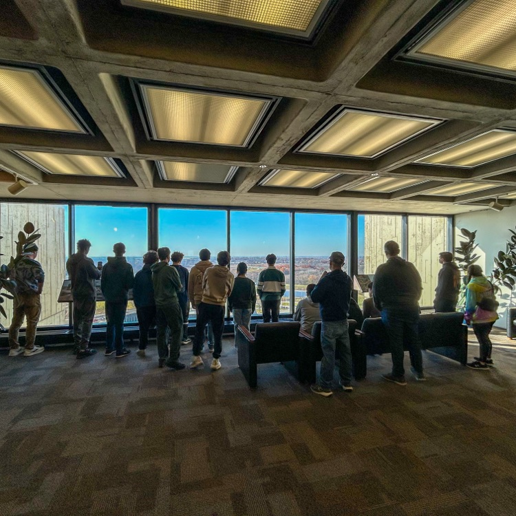 A group of highschool students standing and looking out a window