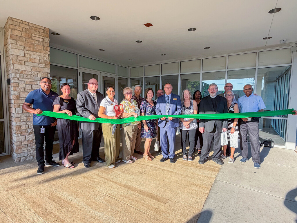 **Alt text:** A group of District 228 Board of Education members, administrators, staff, community leaders, and guests stand outside the Bremen High School District 228 Administration Center holding a green ribbon during the official ribbon-cutting ceremony. The group poses in front of the building's entrance in celebration of the opening of the District's new administrative offices and first-ever board room.