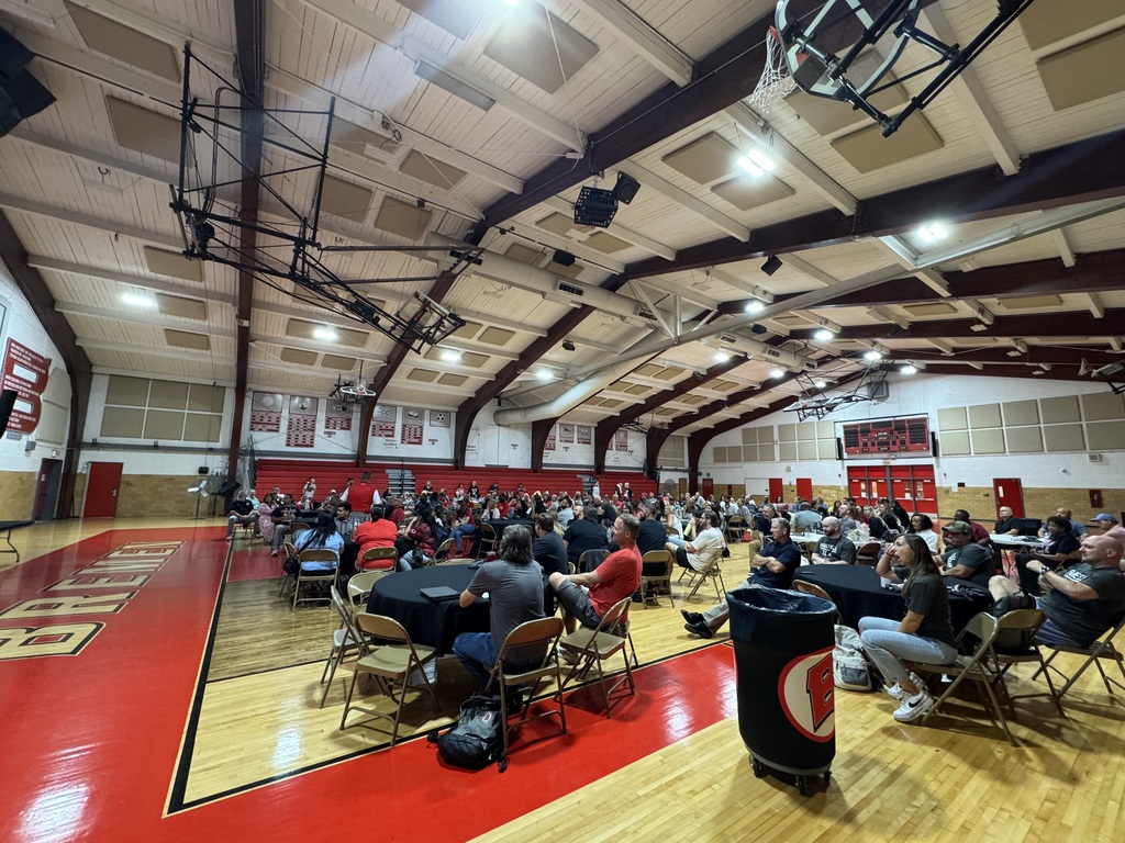 Staff members gather around tables in a high school gymnasium during a districtwide meeting or professional development session.