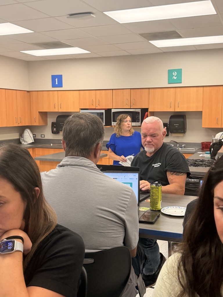 Staff members collaborate in small groups with laptops and notes during a professional development session in a classroom.