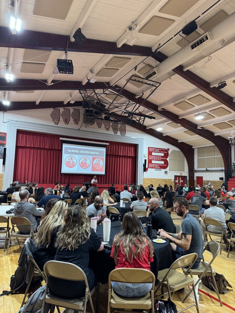 Staff members gather around tables in a high school gymnasium during a districtwide meeting or professional development session.