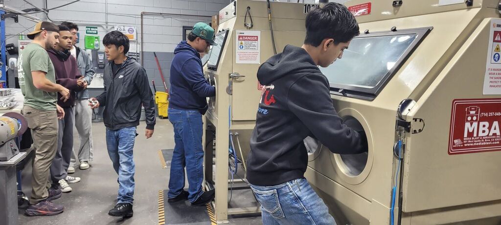 Students speak with employees and examine equipment inside a manufacturing facility.