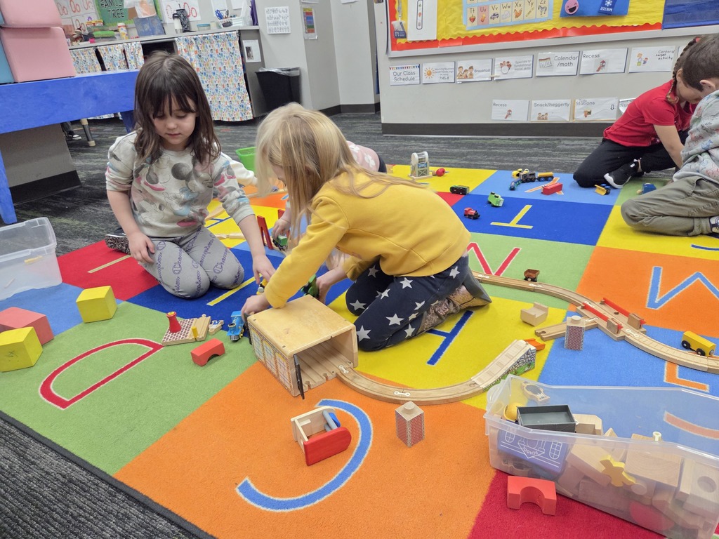 2 girls playing with a wooden train track