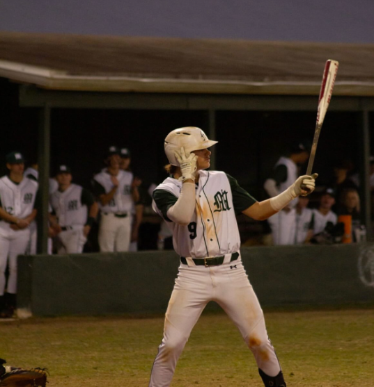 Ready To Swing - Mel High junior Johnny Hemel steps up to the plate during a varsity baseball game at the school field this season. Hemel stood ready in the batter’s box under the lights as his teammates watched from the dugout behind him. The moment captured him preparing to swing in a key at-bat during the game. Hemel showed focus and determination as he competes at the varsity level. “I stay focused, listen to music, and warm up properly,” Hemel said.   Photo By Hunter Paige