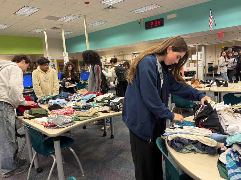 RECYCLING. Charlie Morrissette(9) comes to the swap shop chooses a shirt out of the donations stacks and sees if she likes it. Last Friday, on January 16th Ms.Melanie Anderson helped the Interact club host a Swap Shop. The Swap Shop helped students donate clothes they didn’t like as well as pick something they would prefer using a ticket system. This helped clothes not get thrown out end up in landfills. Darla Sheckler(9), who went to the swap shop with Morrissette said, “I wish clothes were more organized, but I really enjoyed it”. Photo by Aadhya Patel.